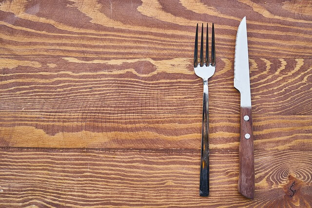 non riesco a dimagrire: Forchetta e coltello su un tavolo di legno. Rappresenta il digiuno.